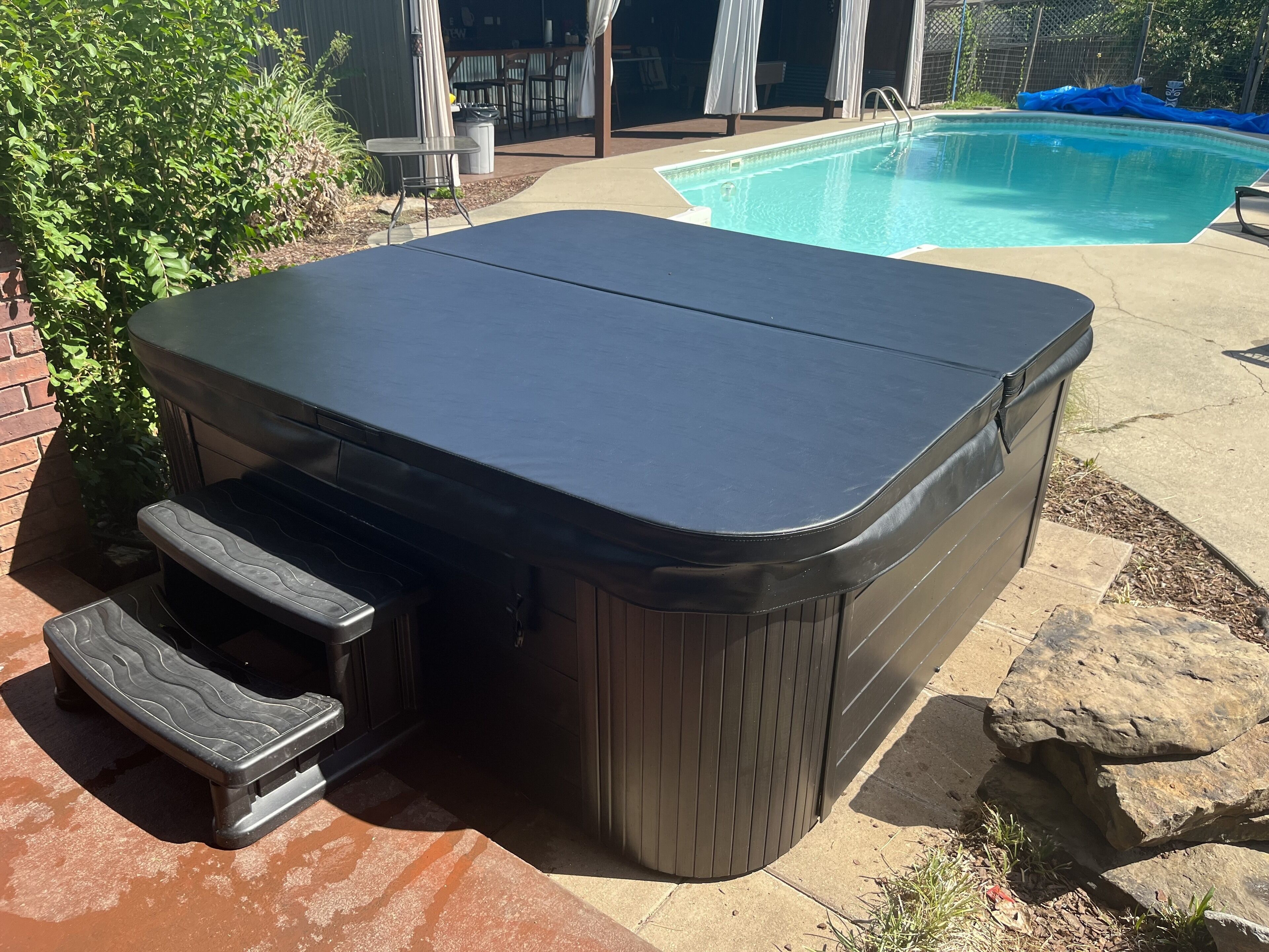A hot tub with a built-in seat and steps, located outdoors near a pool.