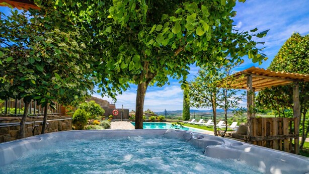 A hot tub surrounded by lush greenery, a pool, and a wooden pergola.