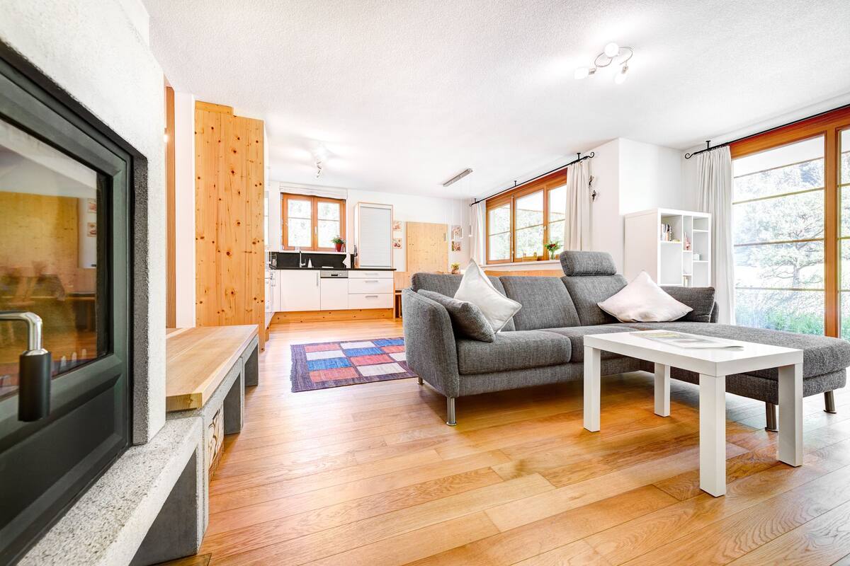Una sala de estar moderna con un sofá gris, una mesa de centro blanca y suelo de madera.