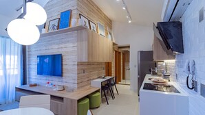 A modern kitchen with a built-in oven, a dining area with a white table and chairs, and a TV mounted on the wall. - Apartamento beira mar - OKA Beach Resort (Ipojuca)
