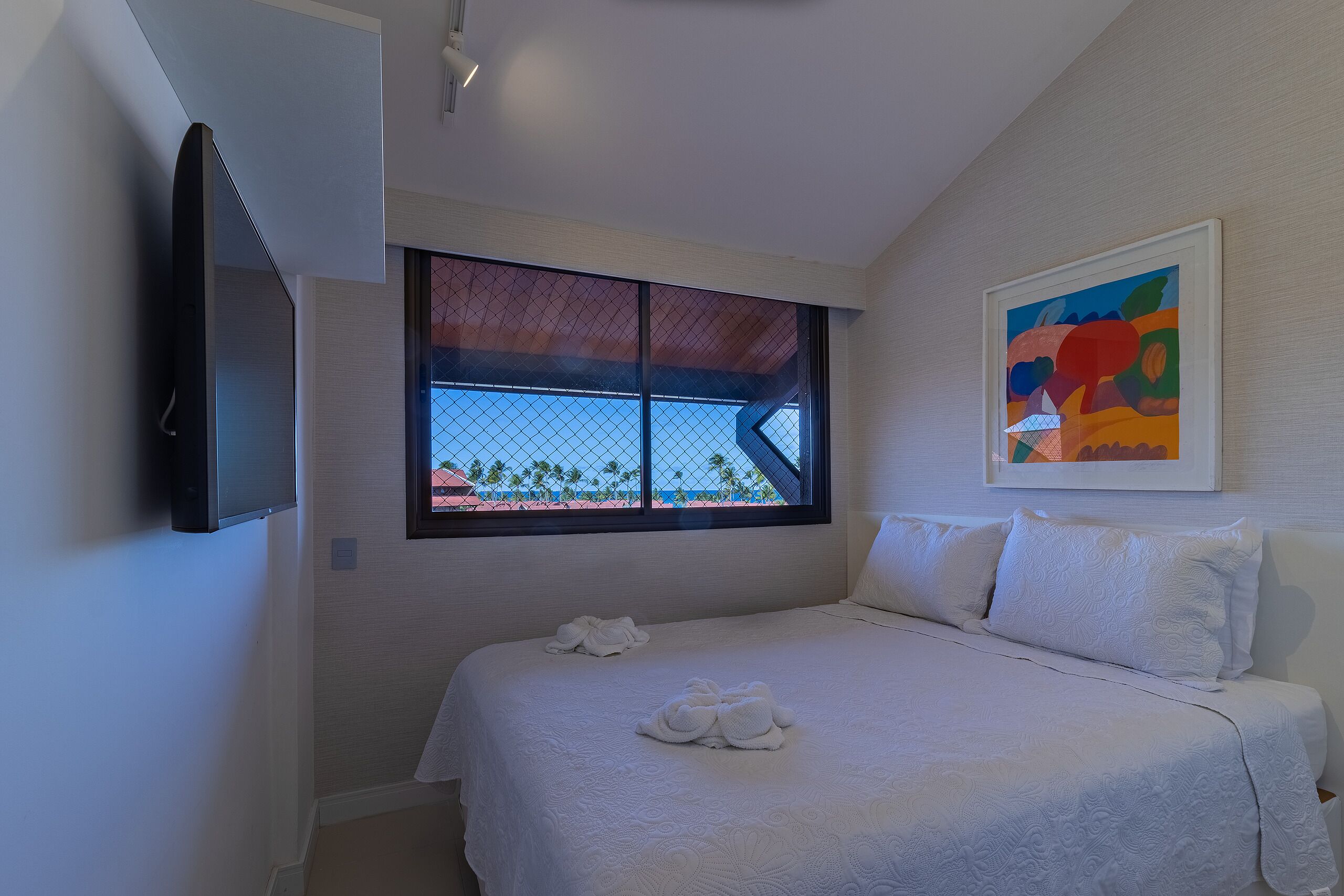 Une chambre à coucher avec un lit, des oreillers, une télévision, une fenêtre donnant sur un beau paysage et un tableau accroché au mur.