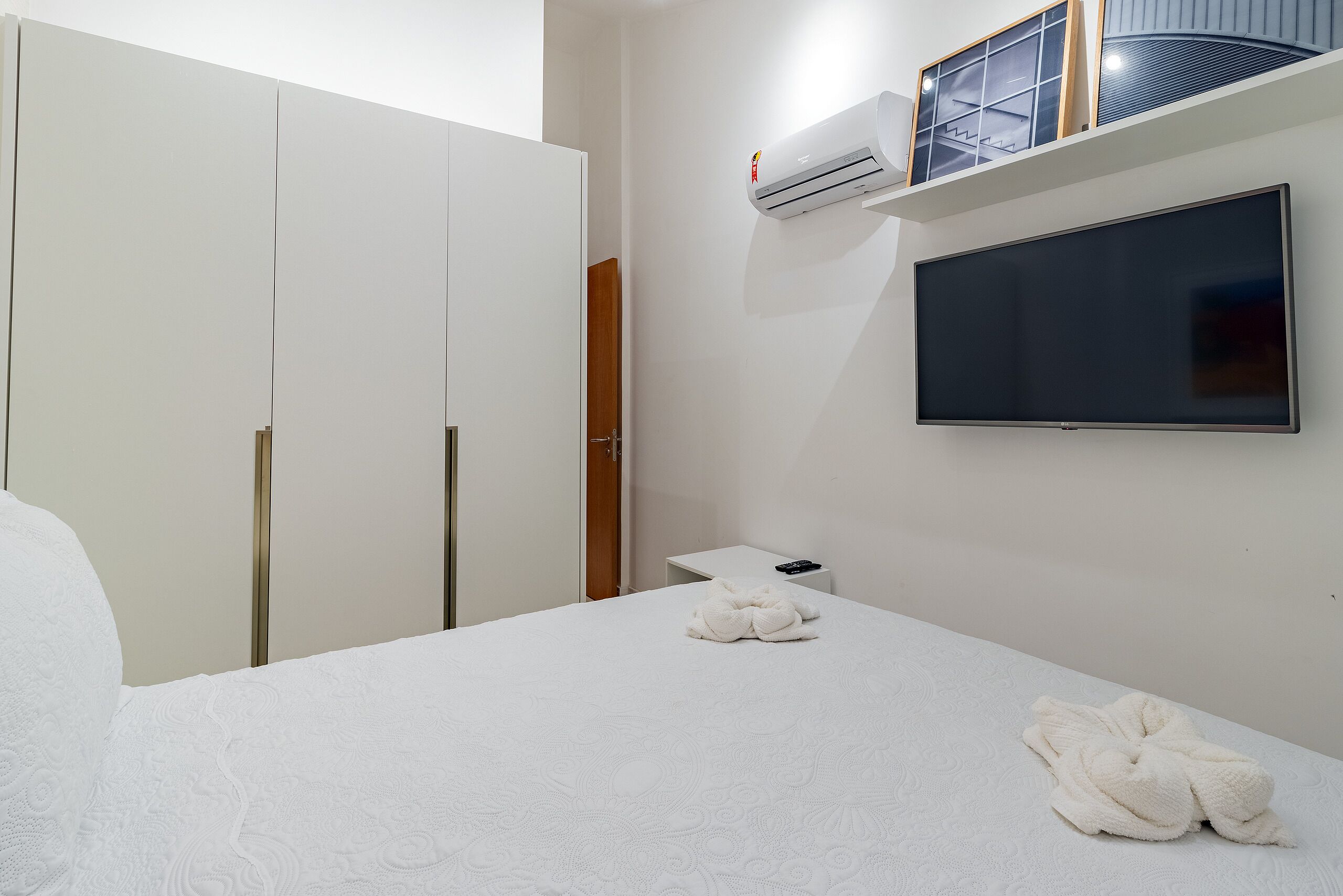 A hotel room with a bed, a TV, a wardrobe, and an air conditioning unit.