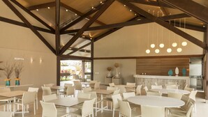 A spacious indoor dining area with multiple tables and chairs, a high ceiling with exposed beams, and hanging pendant lights. - Apartamento beira mar - OKA Beach Resort (Ipojuca)
