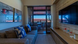 A modern living room with a sofa, a TV, and a view of the outside. - Apartamento beira mar - OKA Beach Resort (Ipojuca)