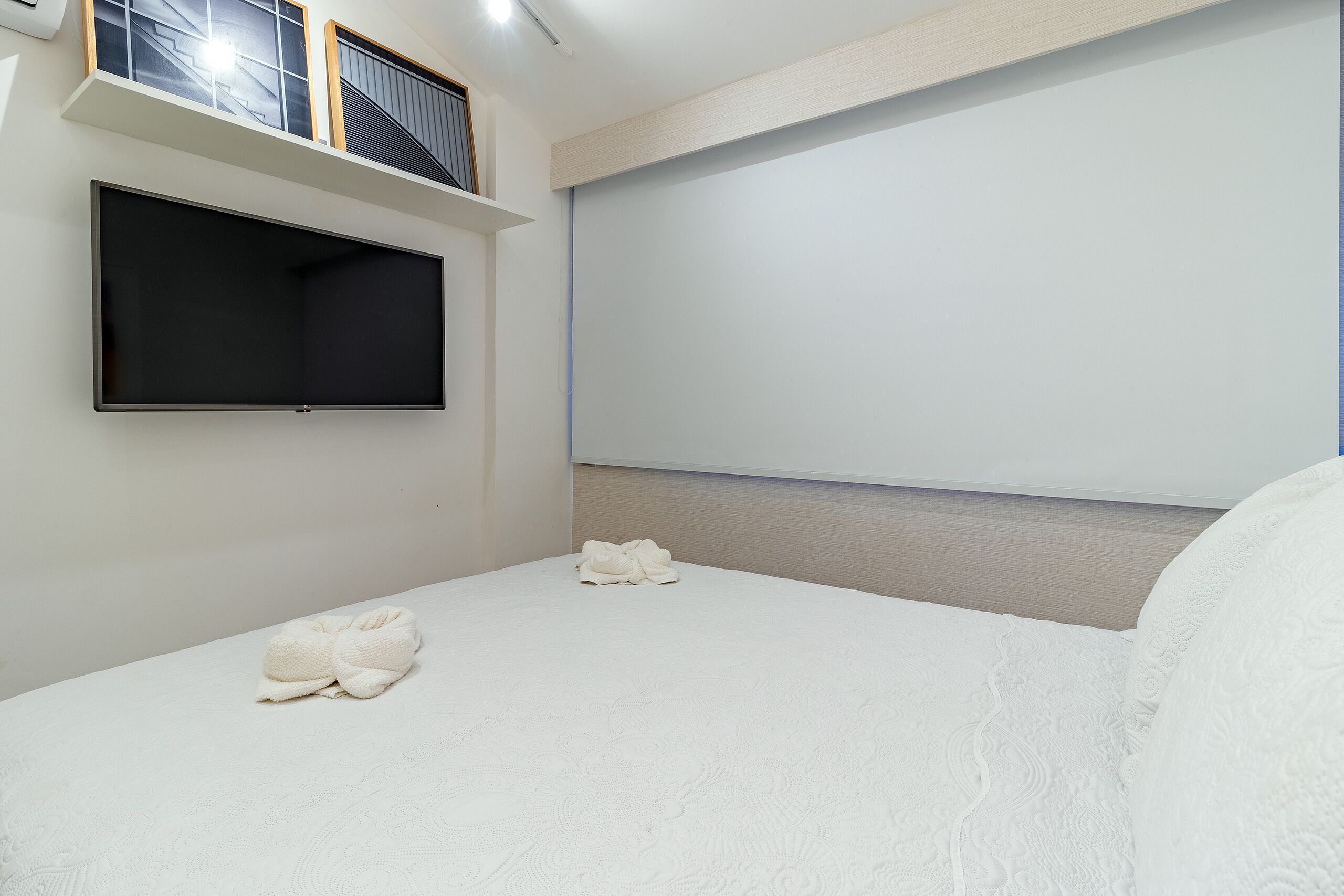 Habitación de hotel con cama, televisor de pantalla plana montado en la pared y ventana con persianas.