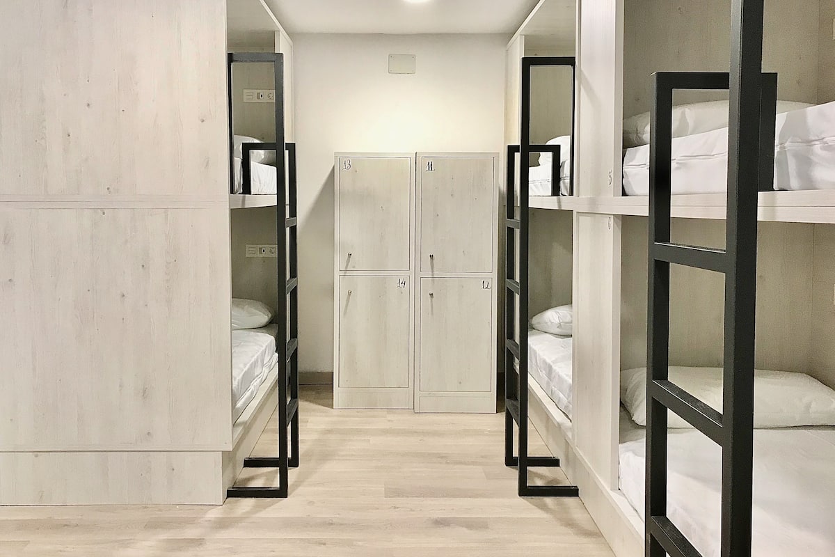 A corridor with bunk beds on both sides, a central wardrobe, and a wooden floor.