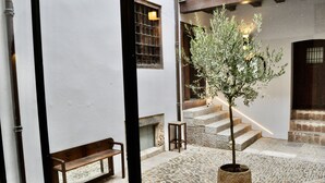 Un patio con suelo de piedra, un banco de madera, un árbol en maceta y una escalera.