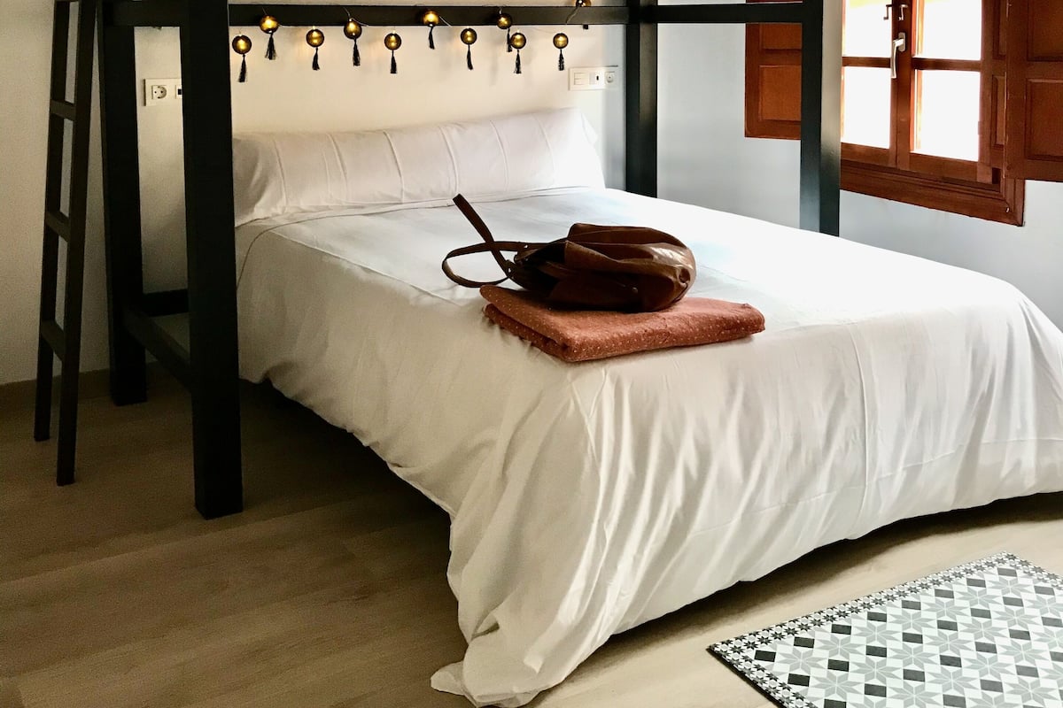 A bunk bed with a white mattress, a brown bag on the lower bunk, and a patterned rug on the floor.
