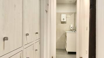 Un pasillo estrecho con casilleros a la izquierda, que conduce a un baño con lavabo y dispensador de jabón.