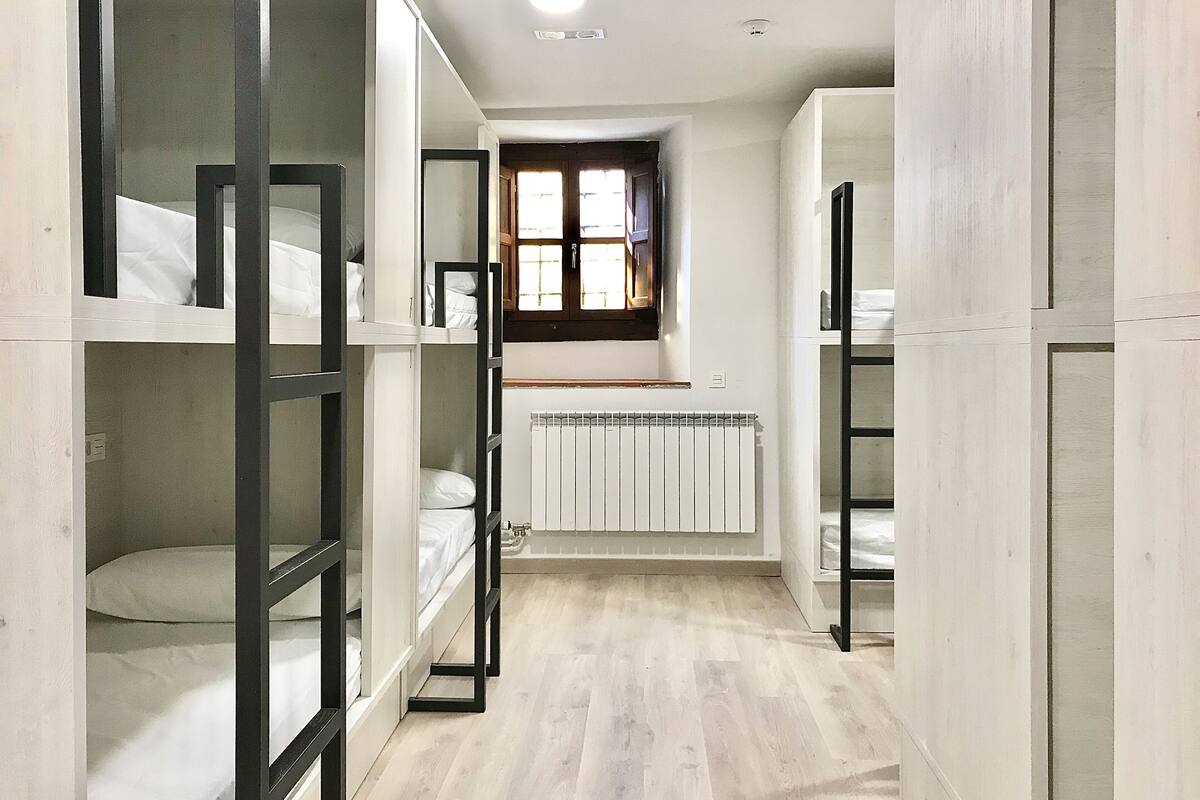 A narrow hallway with bunk beds on either side, a radiator, and a window with a view of the outside.
