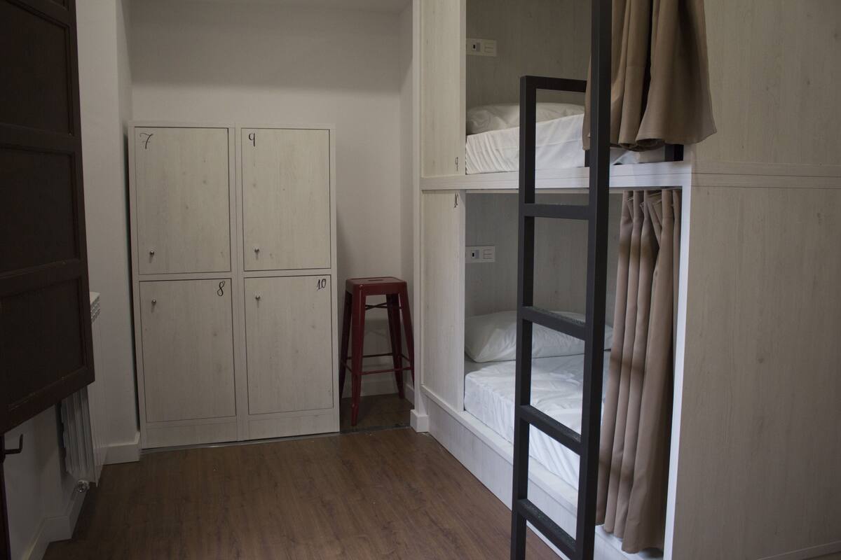 A room with bunk beds, a wooden stool, and a set of white lockers.