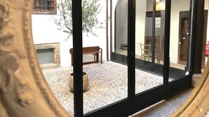 Vista a través de un ventanal hacia un espacio con suelo de piedra, un banco de madera y una planta en maceta.