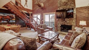 Un salón amplio con chimenea de piedra, sofás de cuero, una mesa de centro de vidrio y una escalera de madera.