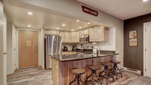 Una cocina con armarios de madera, electrodomésticos de acero inoxidable y una zona de bar con taburetes.