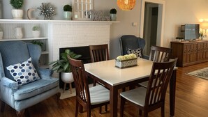 Een eethoek met een wit bakstenen haard, houten stoelen, een tafel en een hanglamp.