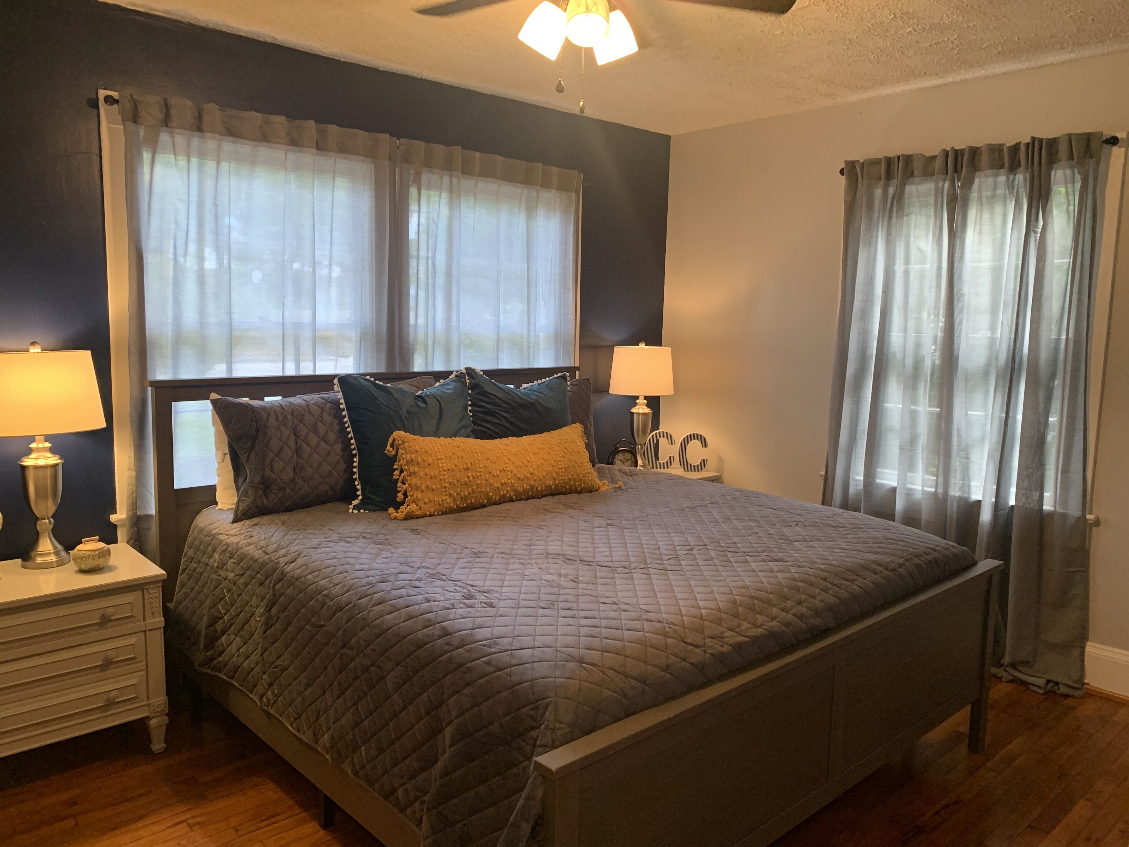 A neatly made bed with a quilted bedspread and several pillows, flanked by bedside tables with lamps and clocks.