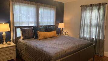A neatly made bed with a quilted bedspread and several pillows, flanked by bedside tables with lamps and clocks.