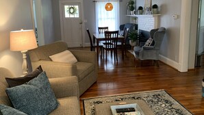 Een woonkamer met een bank, salontafel, lamp, eettafel met stoelen, een open haard en een vloerkleed.