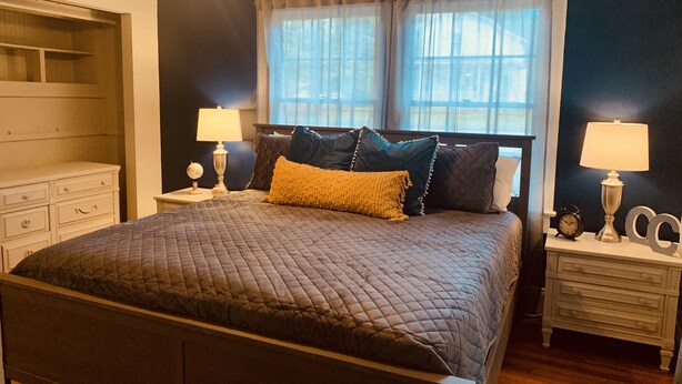 Een slaapkamer met een groot bed, twee nachtkastjes met lampen, een nachtkastje, een dressoir en een raam met gordijnen.