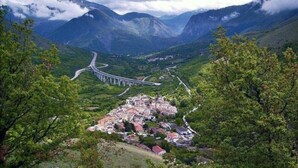 Paesaggio montuoso con una strada tortuosa e un piccolo villaggio con edifici tradizionali.