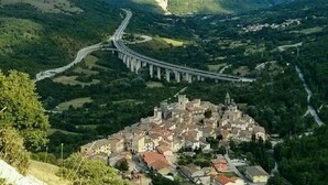 Paesaggio montuoso con una strada tortuosa e un piccolo paese con edifici storici.