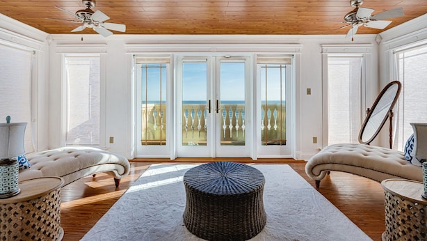 A spacious room with a high ceiling, two ceiling fans, a large window with a view, and a round ottoman in the center. - Latitude Change - Luxury Oceanfront Home (daytona beach)