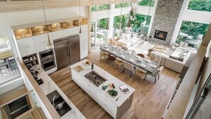 Una cocina moderna con una isla central, vigas de madera, ventanas amplias y una chimenea de piedra.