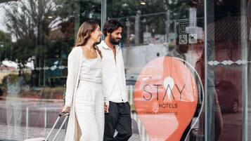 Una pareja de pie frente a la entrada de un hotel con un amplio ventanal.