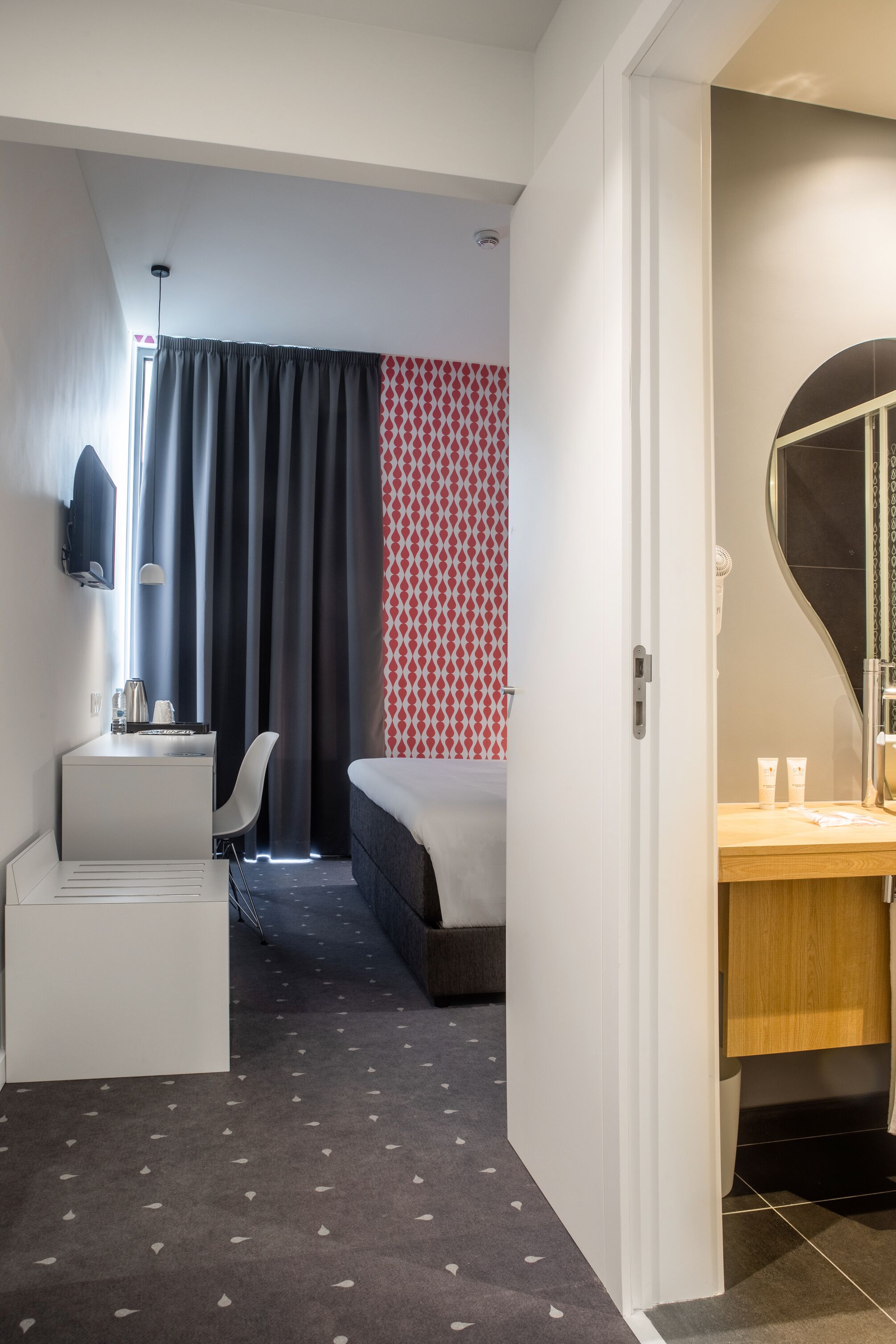 Habitación de hotel moderna con escritorio, silla, cama y baño con espejo y artículos de aseo.