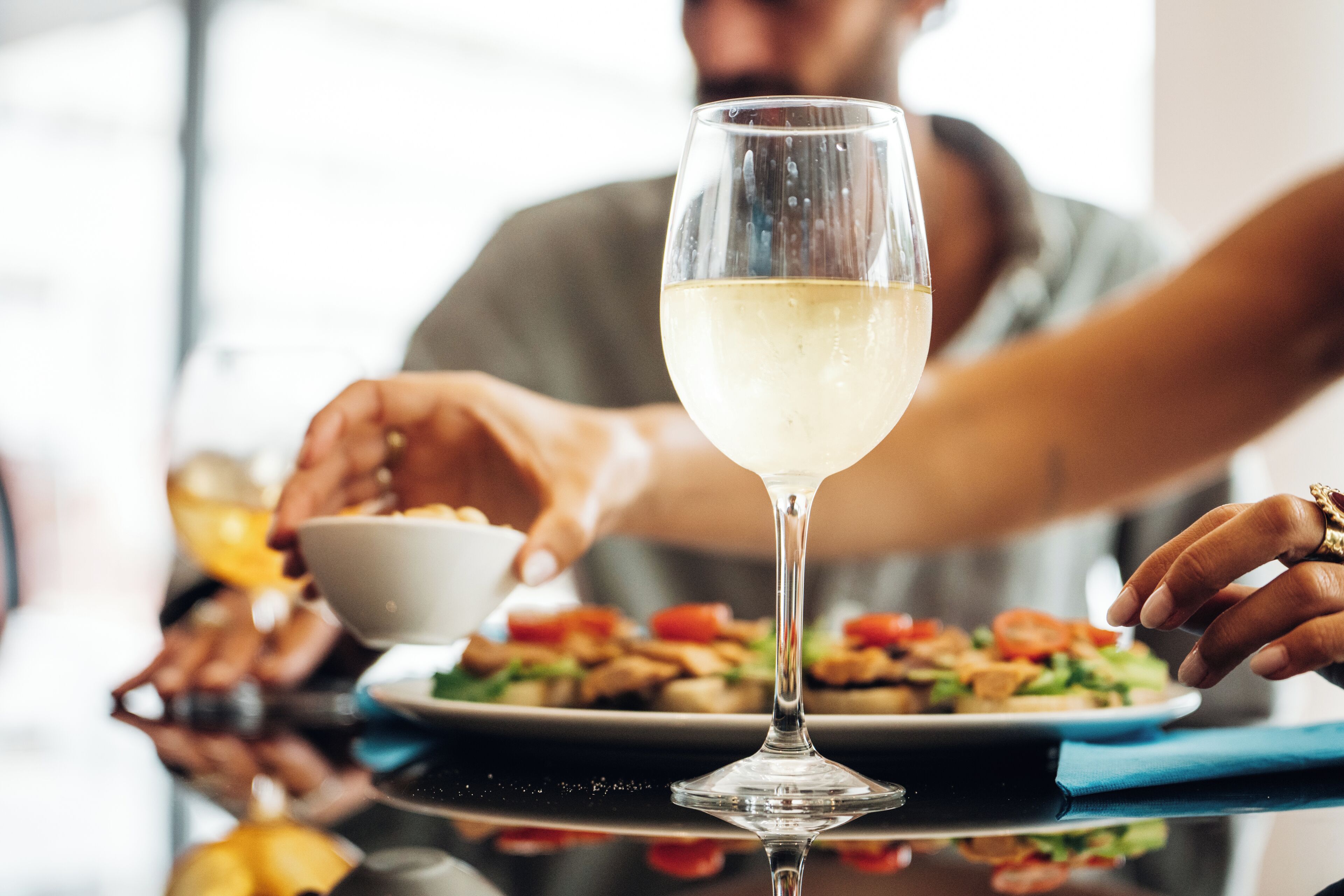 Une table à manger avec un verre de vin blanc, une assiette de nourriture et une personne qui se sert.