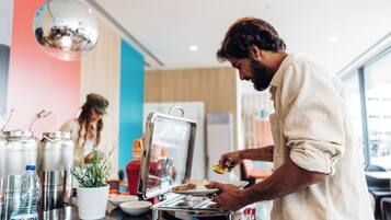 A person serving food at a buffet with stainless steel containers and a potted plant on the counter.