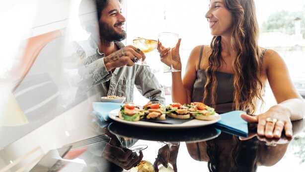 A dining table with a plate of appetizers and a glass of wine.