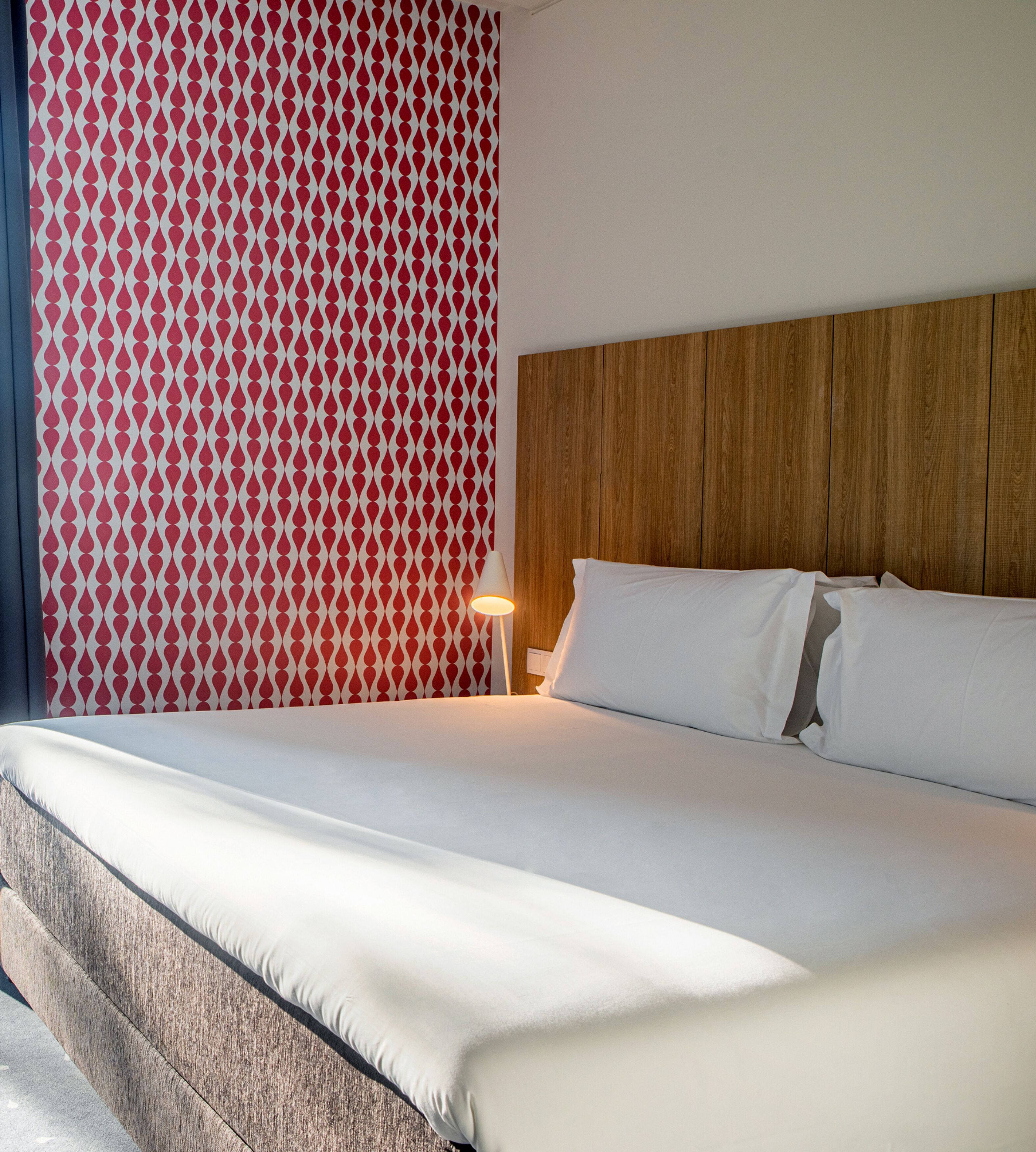 A neatly made bed with white linens, a wooden headboard, and a patterned curtain.