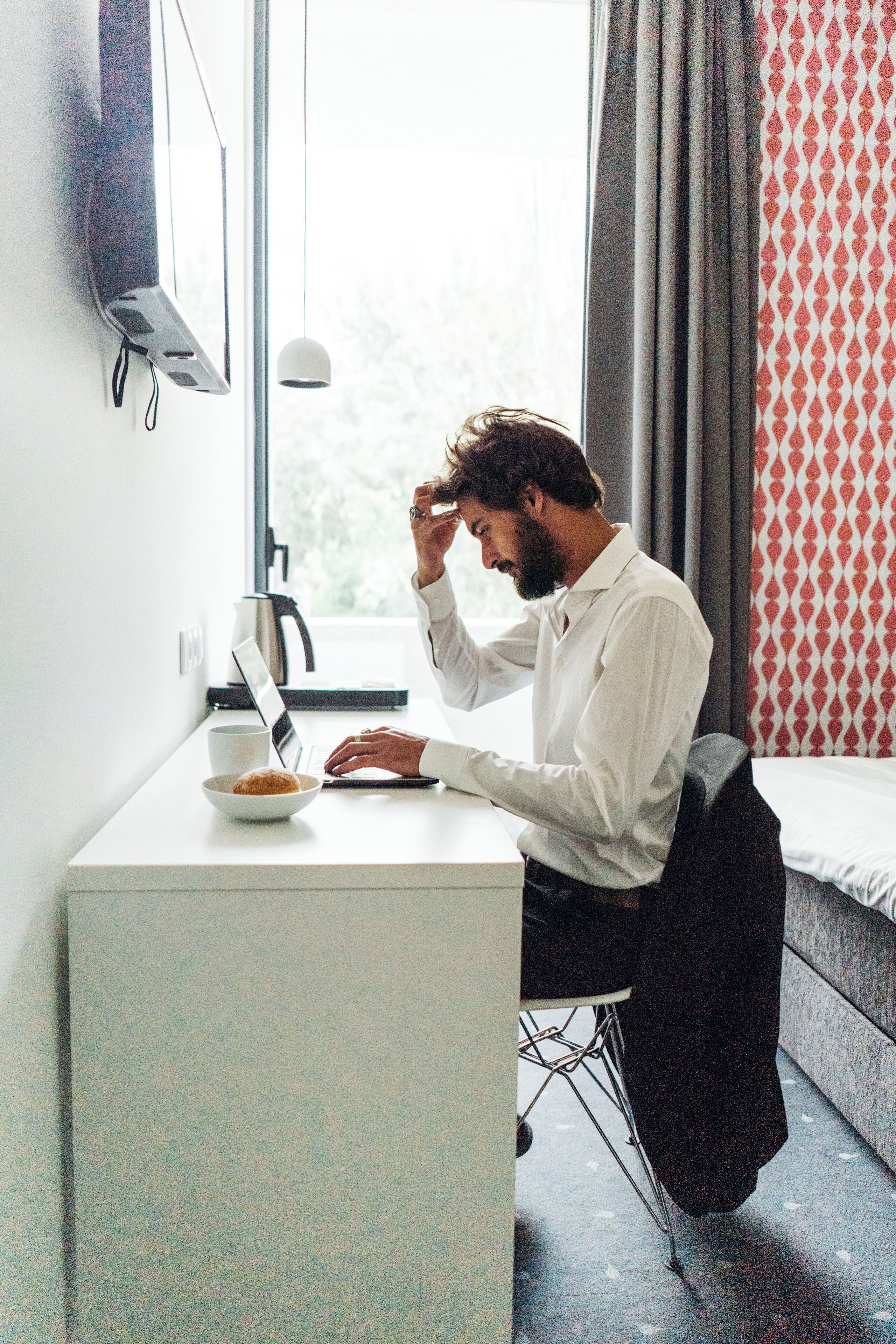 A man sitting at a desk with a laptop, a bowl of food, and a cup.