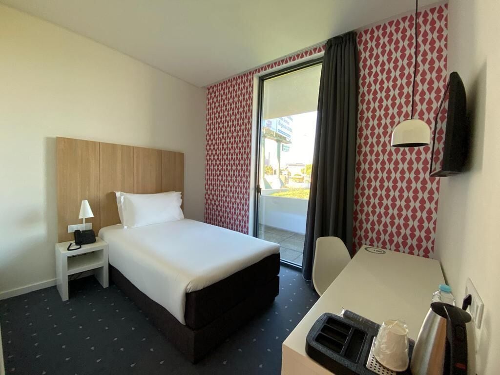 Une chambre d’hôtel avec un lit, un bureau, une chaise, une télévision et une fenêtre avec des rideaux.