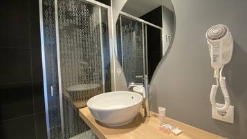 Un baño moderno con un lavabo blanco grande, un secador de pelo portátil y una ducha con puertas de vidrio con diseño.