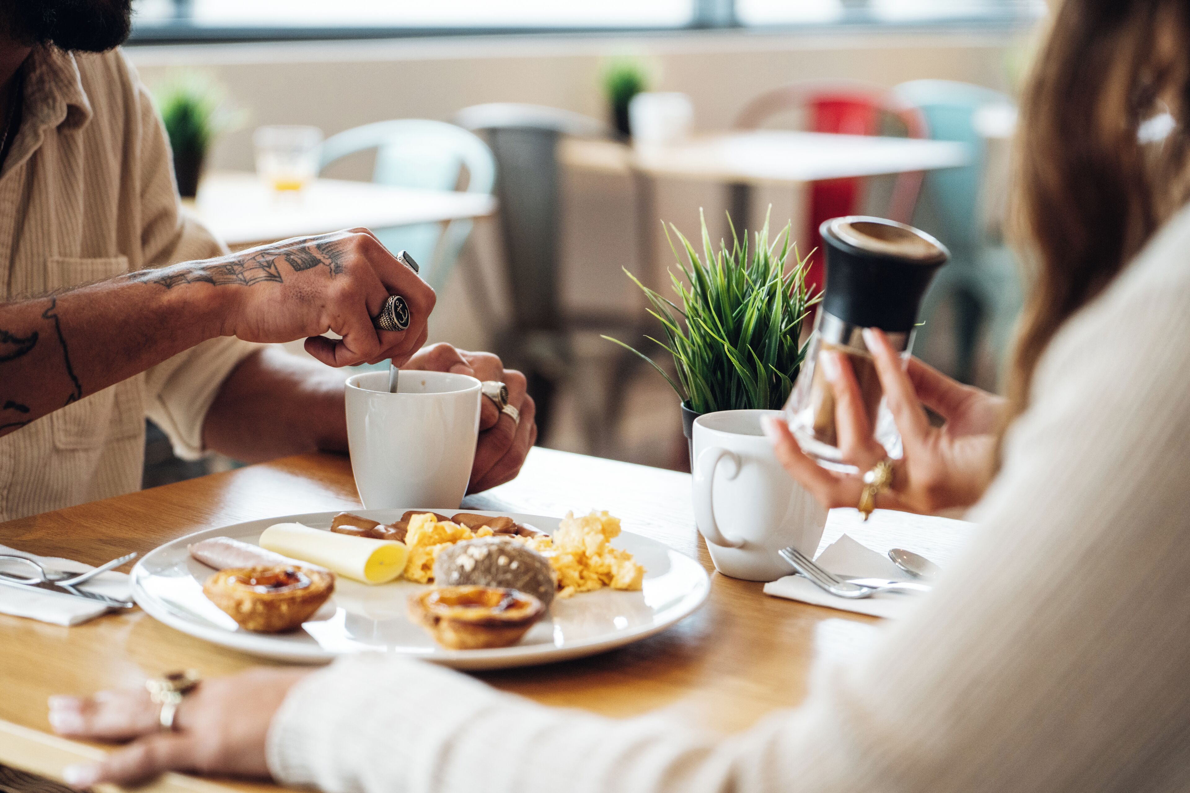 Disposição para o café da manhã, com um prato de comida, uma xícara de café e um pequeno vaso de planta em uma mesa.