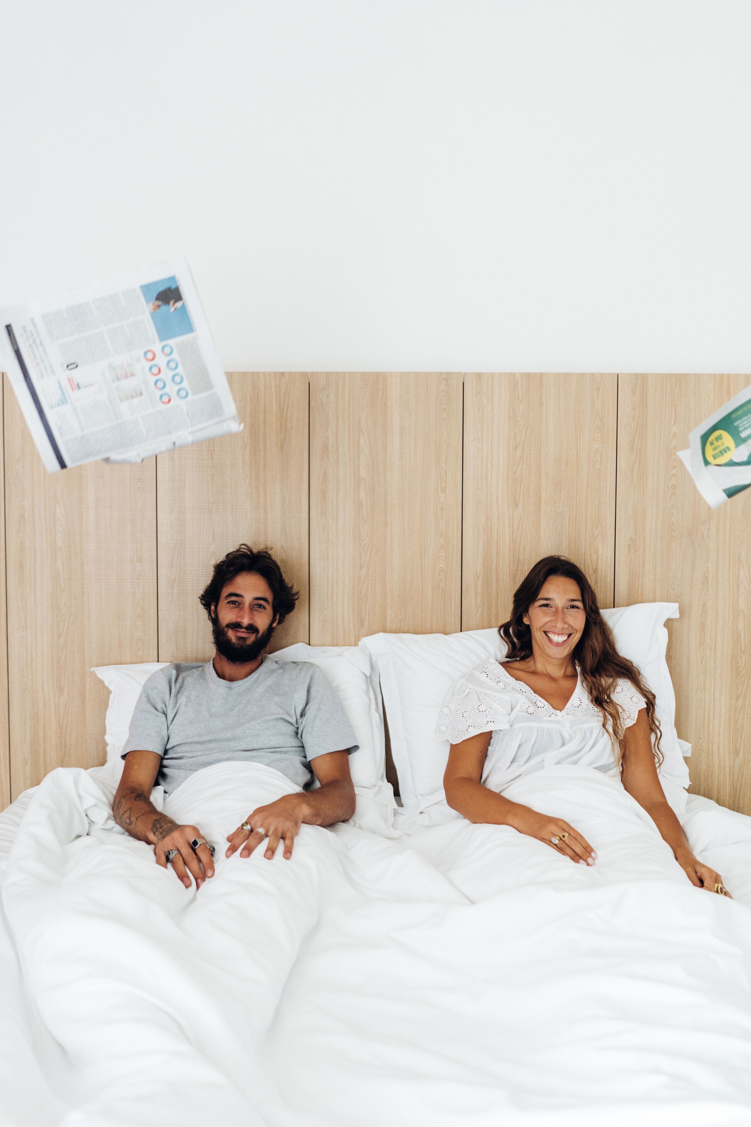 Un dormitorio con cabecera de madera, ropa de cama blanca y una revista sobre la cama.