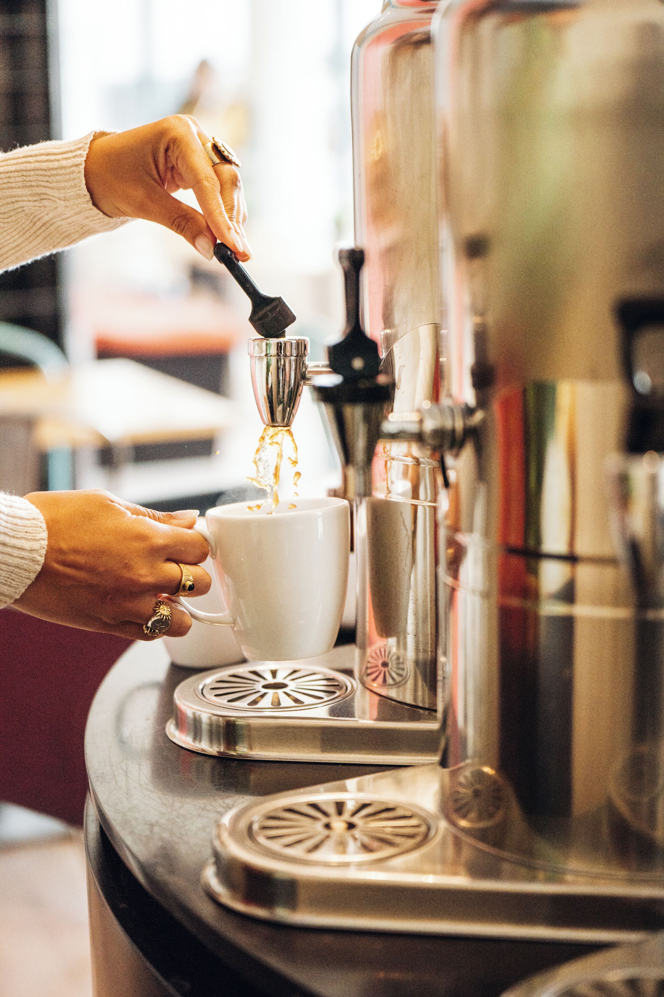 A person pouring coffee into a cup using a coffee machine.