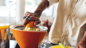 A person squeezing an orange into a bowl.