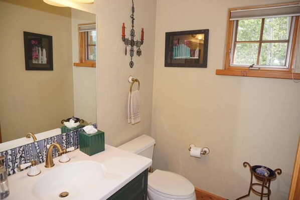 A bathroom with a white sink, a toilet, a mirror, and a window.