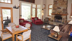 A spacious living room with a fireplace, red sofas, a dining table, and a view of the outdoors. - 24 Little Ln (Snowmass Village)