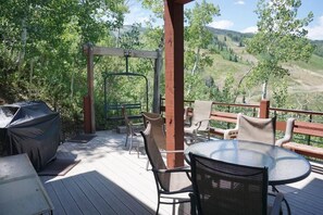 A deck with outdoor furniture, a covered grill, and a swing set overlooking a forested valley. - 24 Little Ln (Snowmass Village)