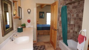 A bathroom with a white sink, a mirror, a clock, and a shower with a green curtain. - 24 Little Ln (Snowmass Village)