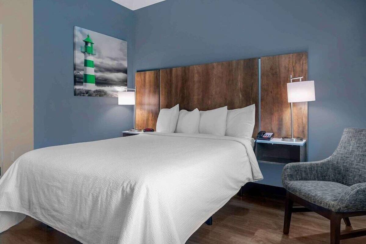 A hotel room with a large bed, a nightstand, a chair, and a painting of a lighthouse.