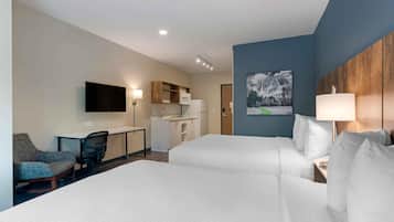 Quarto de hotel com duas camas, uma escrivaninha, uma cadeira, televisão, micro-ondas e um quadro na parede.
