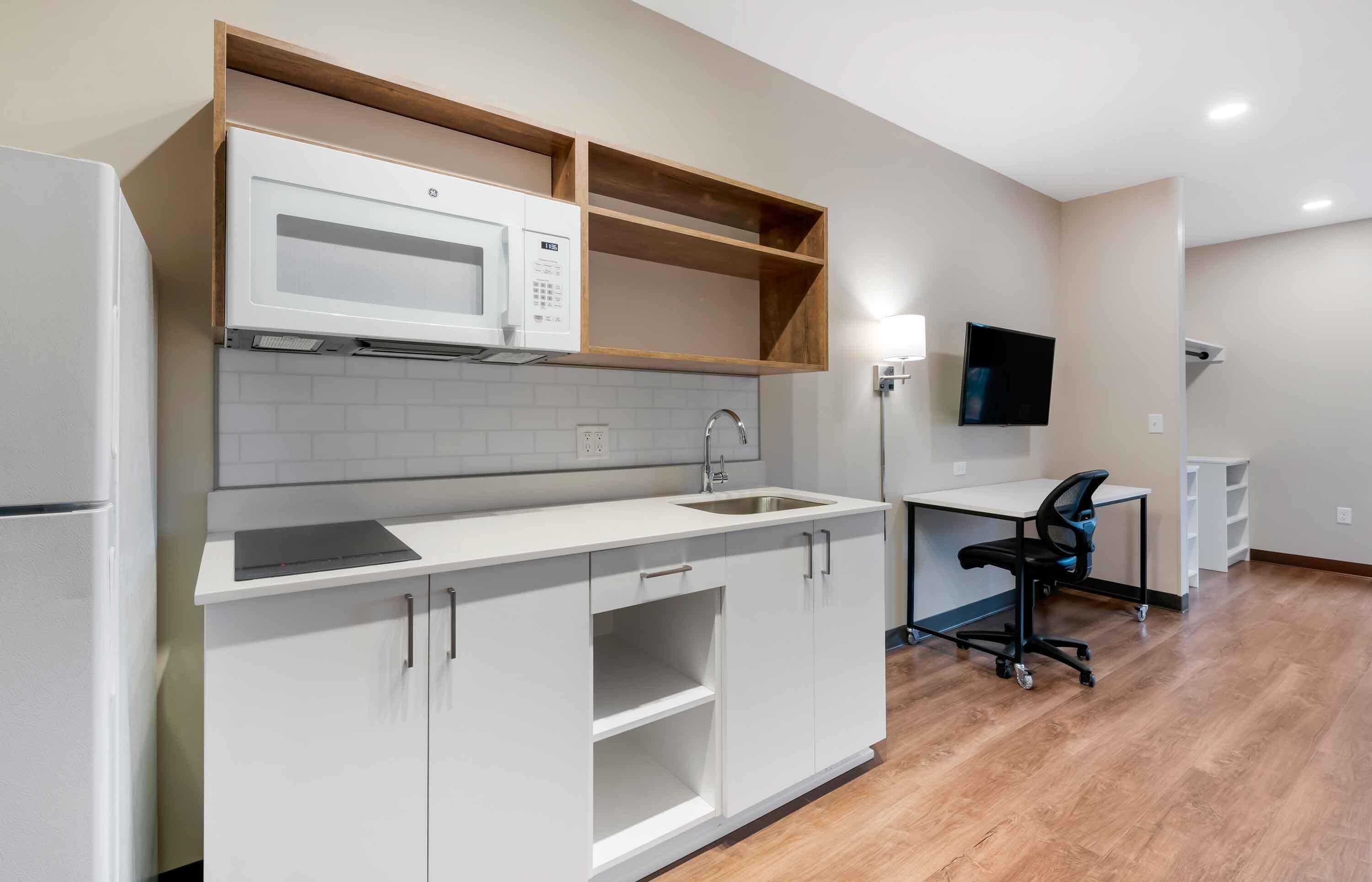 Una cocina moderna con armarios blancos, un microondas, un lavabo y una estantería de madera.