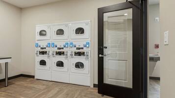 A laundry area with multiple washing machines and dryers, a door with a fire alarm, and a small table.