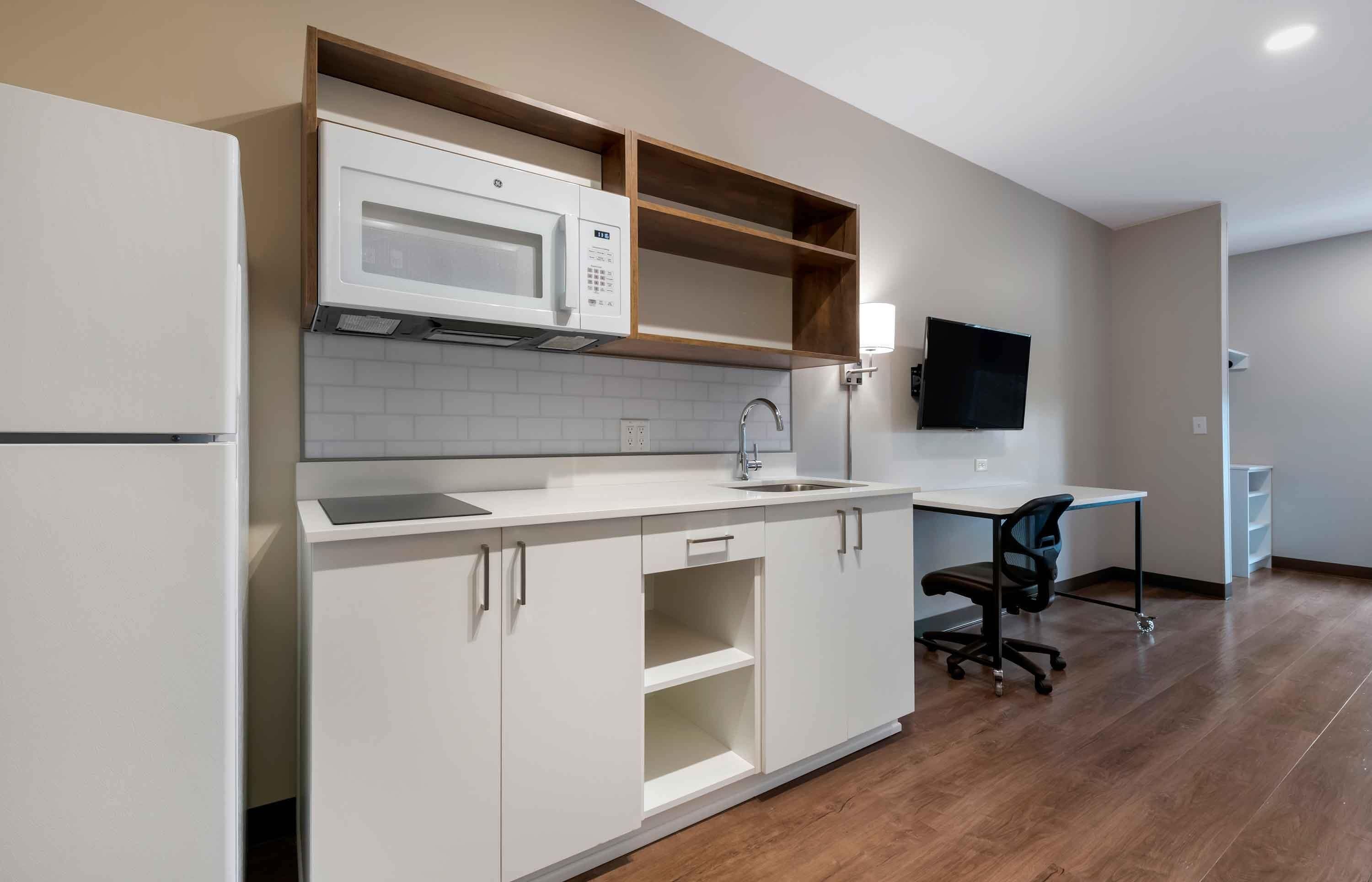 A modern kitchen with white cabinets, a microwave, a sink, and a flat-screen TV mounted on the wall.