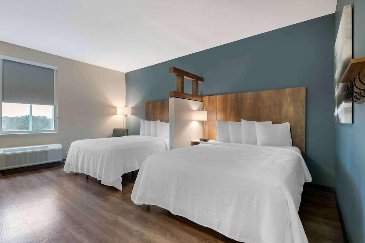 A hotel room with two beds, a large window, a radiator, and a wooden headboard.